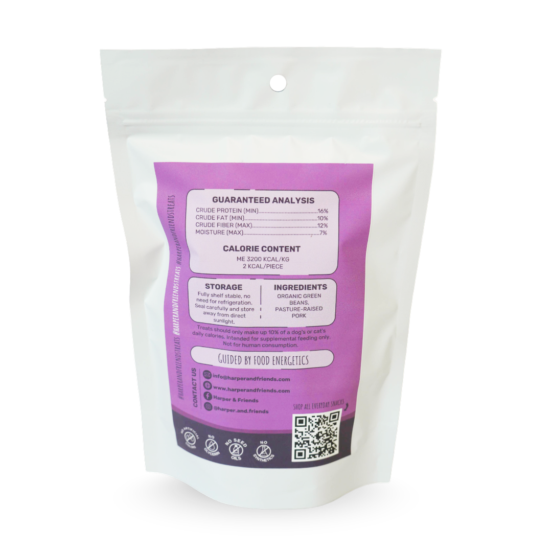 A white stand-up pouch of green bean pet treats with a large purple label showing guaranteed analysis, calorie content, storage, and ingredients. The brand name &