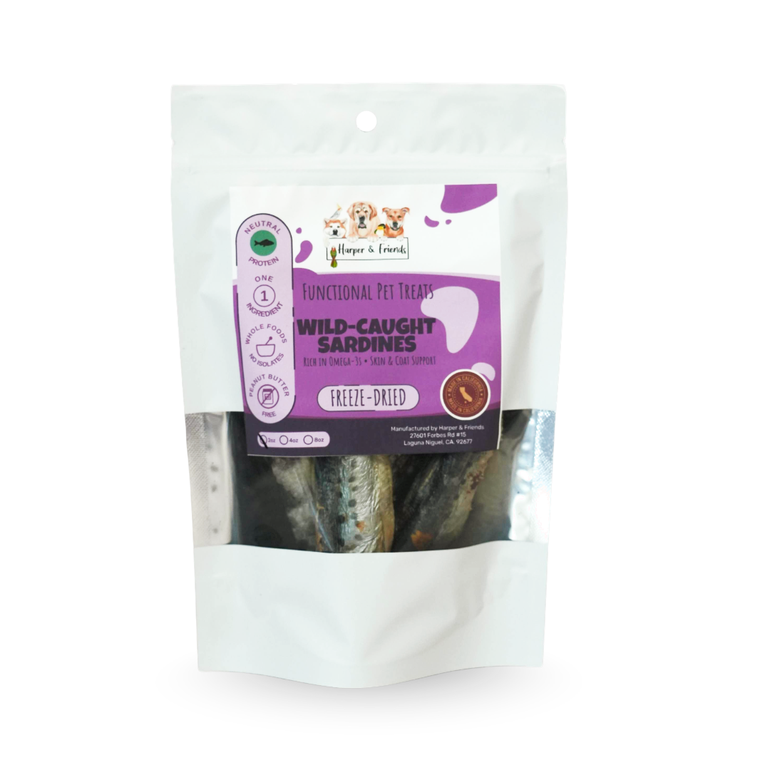 A white stand-up pouch of dog treats with a clear window showing freeze-dried sardines inside. The front label reads &