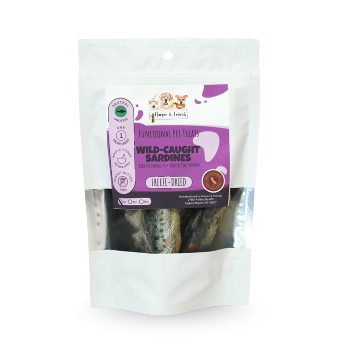 A white stand-up pouch of dog treats with a clear window showing freeze-dried sardines inside. The front label reads &