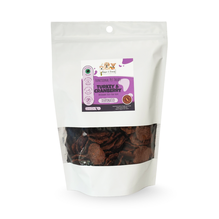 A white stand-up pouch of functional pet treats, specifically Turkey &amp; Cranberry, with a clear window showing the dark brown disc-shaped treats inside. The front label features purple and white graphics with the brand logo &
